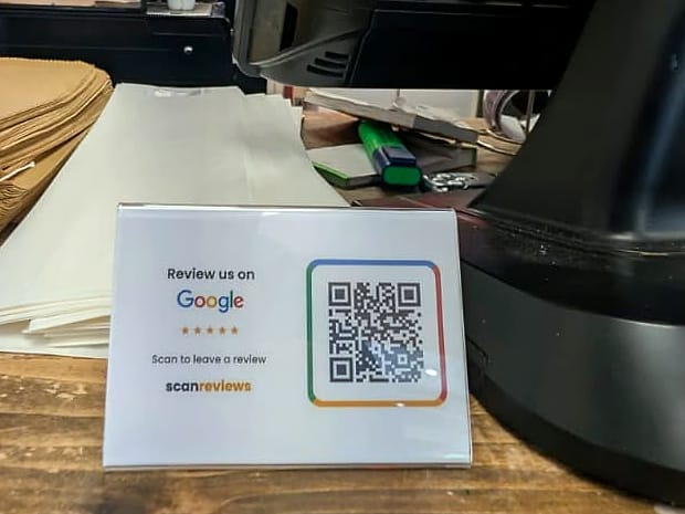 A ScanReviews Google review card on the wooden serving counter of a coffee shop next to the till