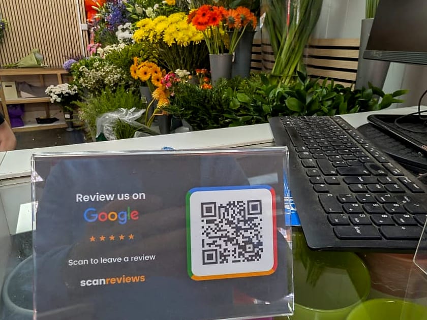 A ScanReviews Google review card at a florist till point with flowers filling the shop behind