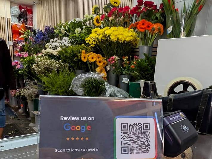 A ScanReviews Google review card on a florist and gift shop counter beside the card machine