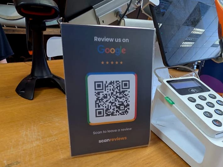 A ScanReviews Google review card on a gift shop sales desk beside a card reader and barcode scanner