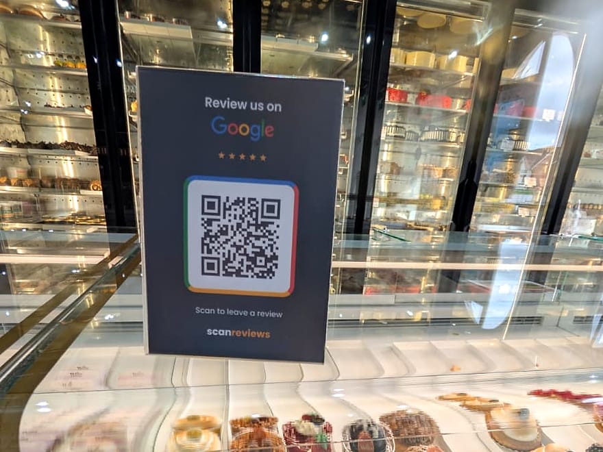 A ScanReviews Google review card on the glass dessert counter of a patisserie above a row of cakes